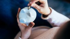 A woman's hands hold a piggy bank while putting a coin into it.